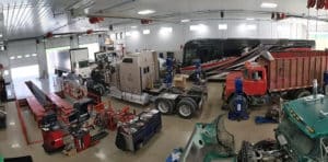 Fleet Maintenance & Why It is Important | Mast Service Center in Etna Green, IN. Buses and trucks undergoing fleet repair or maintenance in an auto repair facility.