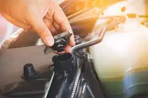 Prepare Your Car's Cooling System Before the Seasons Change | Mast Service Center Inc. Closeup image of a mechanic’s hand opening the radiator cap to check the coolant level of the car radiator.