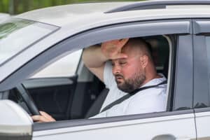 Man driving car without air conditioning while wiping his sweat. Concept image of “How to Keep Any Vehicle Cool and Safe During Hot Months” | Mast Service Center in Etna Green, IN.
