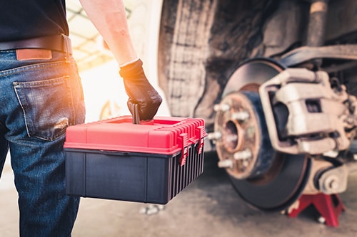 A technician holding a toolbox with blurred disc brakes in the background. Concept image of “6 Things to Know About Truck Brakes” | Mast Service Center in Etna Green, IN.