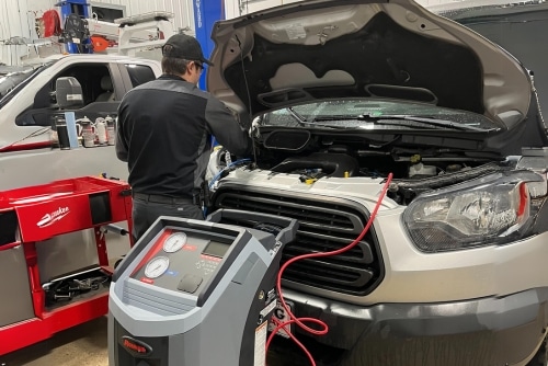 Auto Air Conditioning Repair near me in Etna Green, IN at Mast Service Center. Image of technician undergoing Auto Air Conditioning repair using Robinair 1234yf Refrigerant on an white open hood ford SUV