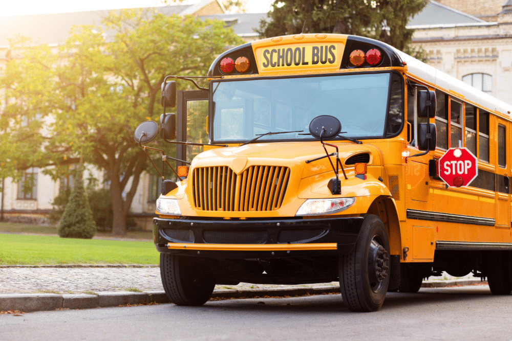 bus repair in Nappanee, IN at Mast Service Center. Bright yellow school bus parked on a street with its stop sign extended, in front of a building and trees in the background.