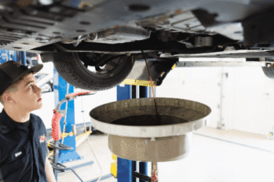 Fluid services by Mast Service Center. Image of a technician draining automotive fluid from a raised vehicle into a large collection pan during maintenance in Etna Green, IN.